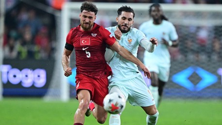 Two soccer players competing for the ball during a match with the player in red representing Turkey.