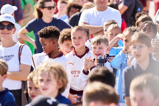 A group of youths, some clapping, dressed in football uniforms at an outdoor event. Faces are blurred.