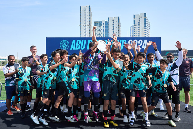 A Manchester City youth team celebrating their victory at the Abu Dhabi Cup 2024, with players wearing medals and holding a trophy.