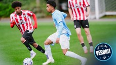 Two young soccer players, one in a blue kit and the other in a red and white striped kit, competing for the ball on a field.