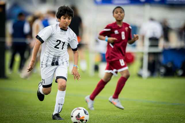 Youth soccer match with players in white and red jerseys actively pursuing the ball on a grassy field.