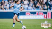 A Manchester City Women's player in action on the field wearing a light blue kit. The backdrop shows a crowd. There's a graphic stating Adobe Women's FA Cup Winners 2026.