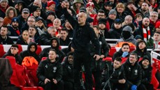 A sports coach or manager gestures energetically at the sideline, surrounded by a focused crowd in a stadium.