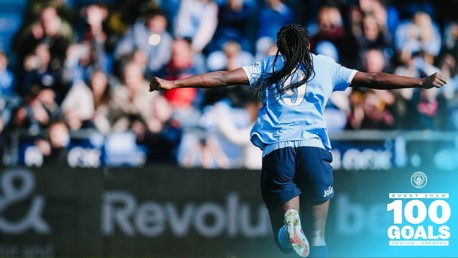Footballer celebrating a milestone of 100 goals from the 2021/22 season to present. The player is in a blue and white kit with number 9, arms outstretched towards a cheering crowd.