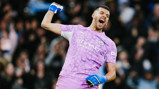 A football goalkeeper in a purple Manchester City kit celebrates with a clenched fist.