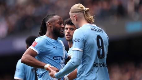 Two Manchester City football players wearing light blue kits with the Etihad Airways logo. One player's jersey reads 'Haaland' with number 9. The scene appears to be a celebration or interaction during a match.