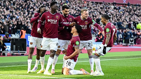 West Ham United players celebrating a goal on the field, wearing maroon jerseys with a crowd in the background.