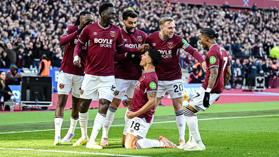 West Ham United players celebrating a goal on the field, wearing maroon jerseys with a crowd in the background.