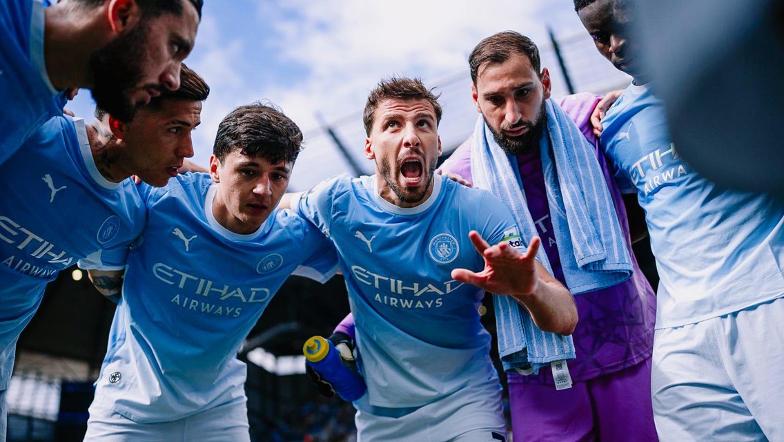 Manchester City players in a team huddle wearing their light blue Puma jerseys with Etihad Airways sponsorship.