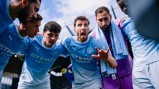 Manchester City players in a team huddle wearing their light blue Puma jerseys with Etihad Airways sponsorship.