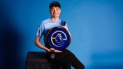 A person in a Manchester City jersey holding an ePremier League champion shield against a blue background.
