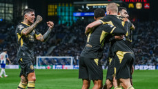 Manchester City players celebrating a goal in dark jerseys with yellow accents during a soccer match.