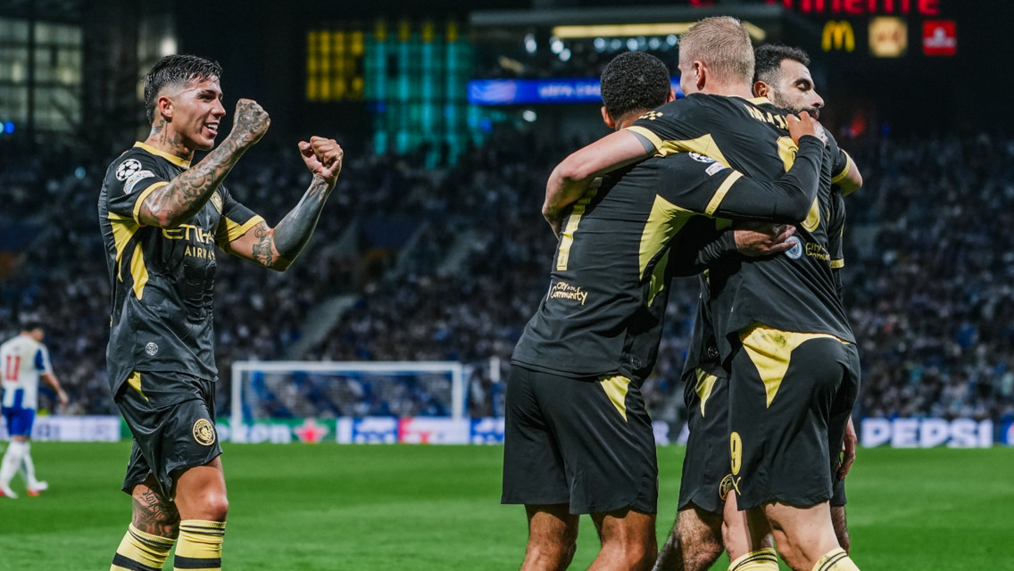 Manchester City players celebrating a goal in dark jerseys with yellow accents during a soccer match.