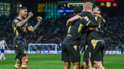 Manchester City players celebrating a goal in dark jerseys with yellow accents during a soccer match.