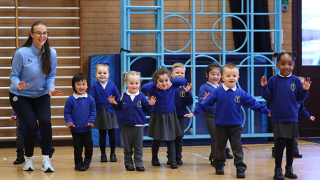 A group of children in blue school uniforms and a coach, participating in a physical activity in a gymnasium.
