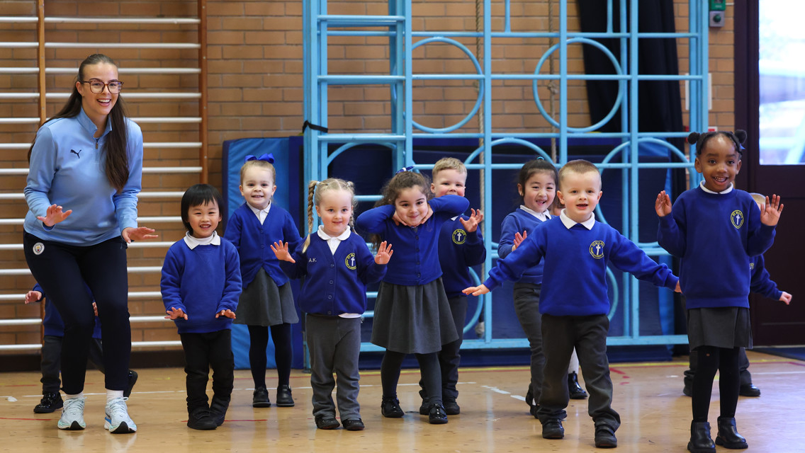 A group of children in blue school uniforms and a coach, participating in a physical activity in a gymnasium.