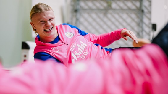 A Manchester City player wearing a pink training bib with the number 9 on it, featuring the club's logo and the Asahi Super Dry sponsor logo.