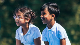 Two children sitting outdoors wearing white polo shirts.