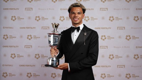 Person in a black tuxedo holding a PFA Player of the Year 2026 trophy at an awards event.
