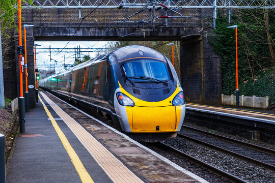 A high-speed train traveling on railway tracks approaching a station under a bridge.