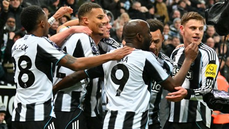 Newcastle United players celebrating a goal during a match. The team's logo and sponsor can be seen on their jerseys.