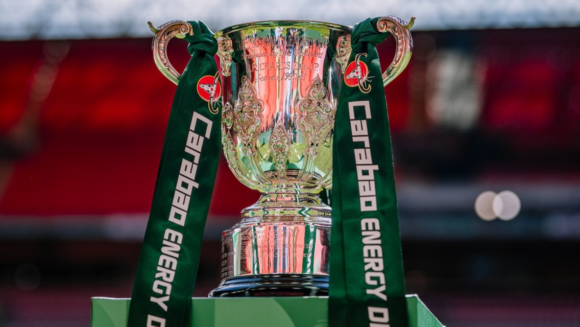 The Carabao Cup trophy with green Carabao Energy Drink ribbons displayed at a stadium.