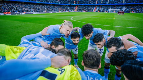 Manchester City players in a huddle on a football field, preparing for a match.