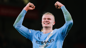 A Manchester City player celebrating a goal with arms raised, wearing the team's blue kit featuring the Etihad Airways logo.
