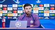 A Manchester City football player at a press conference with a UEFA Champions League background.