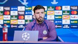 A Manchester City football player at a press conference with a UEFA Champions League background.