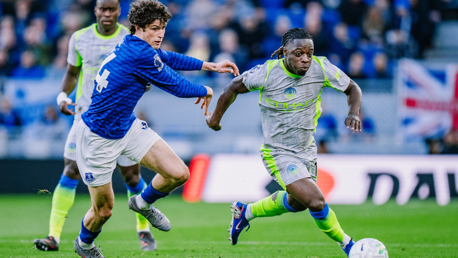 Two soccer players, one in blue and one in gray, are competing for the ball on the field.