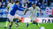 Two soccer players, one in blue and one in gray, are competing for the ball on the field.