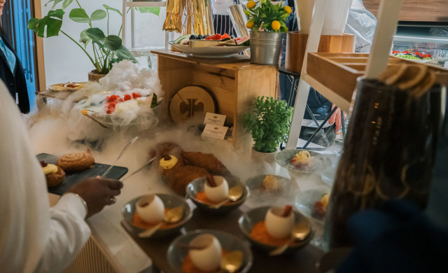 A buffet setup with pastries, bowls containing desserts, and a fruit platter surrounded by decorative fog.