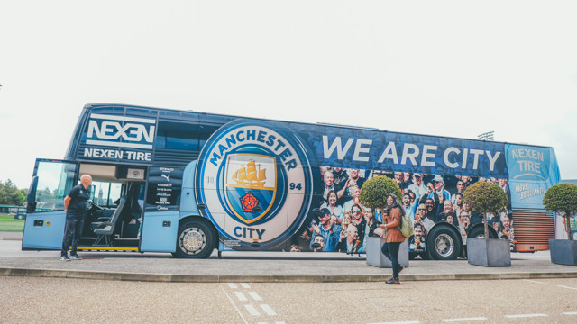 A Manchester City FC team bus featuring the club's logo, the message 'WE ARE CITY' and Nexen Tire branding, parked outdoors with people nearby.