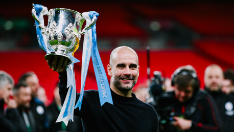 A person holding the Carabao Cup trophy with celebratory ribbons in a sports stadium.