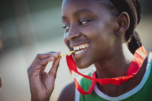 Smiling athlete holding a gold medal with red ribbon in hand, wearing a sports jersey.