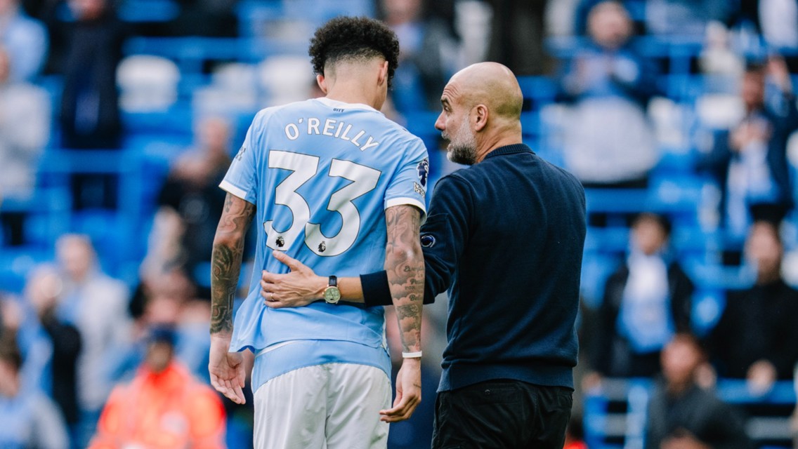 A Manchester City player in jersey number 33, named O'Reilly, being guided by a coach in a stadium setting.