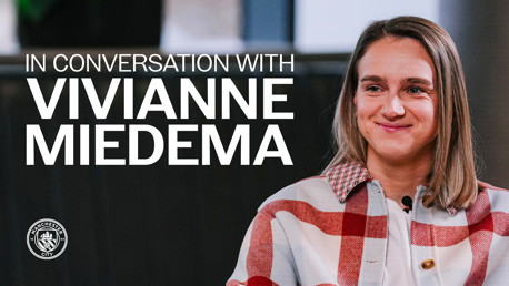 Blurred image of a person in a red and white checkered outfit with the text 'In Conversation With Vivianne Miedema' and Manchester City's logo.