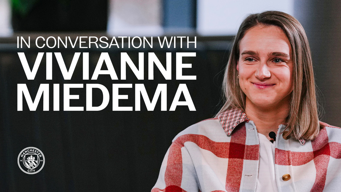 Blurred image of a person in a red and white checkered outfit with the text 'In Conversation With Vivianne Miedema' and Manchester City's logo.