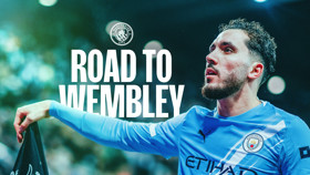 A promotional image featuring Manchester City with text 'Road to Wembley.' The team logo is visible on the blue kit.
