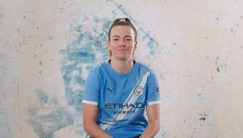 A person wearing a Manchester City football shirt sits against a blue and beige abstract background.