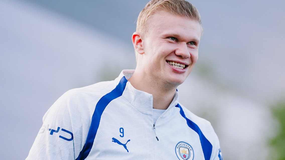 Smiling football player wearing Manchester City training jacket with club crest and Puma logo, outdoors.