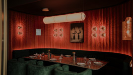 Luxurious restaurant booth with red velvet walls, modern lighting, and green velvet chairs around a set dining table.