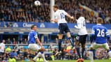 Football match action with Everton and Manchester City players competing for the ball during a Premier League game at Goodison Park. Players are in motion surrounding the ball in the air, with the crowd watching in the background.