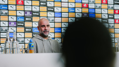 Person in a hoodie at a press conference with sponsor logos on the background wall.