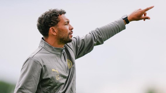 A person in a gray Puma jacket pointing while standing on a pitch.