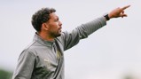A person in a gray Puma jacket pointing while standing on a pitch.