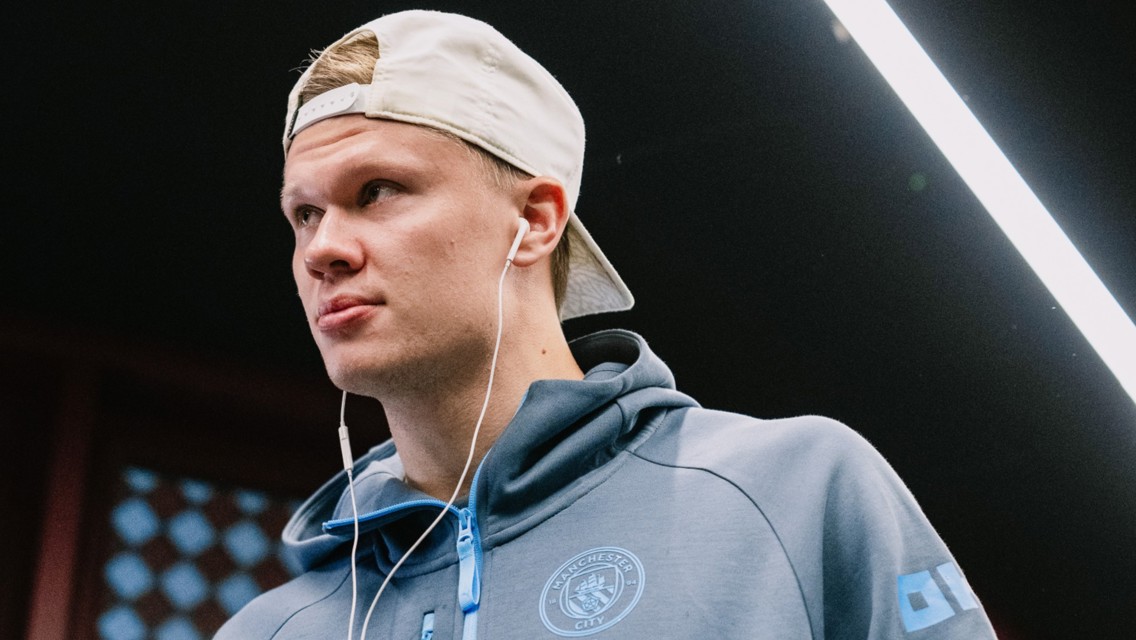Person in a Manchester City hoodie wearing a backward cap and earphones.