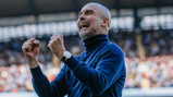 A person in a blue turtleneck celebrating with clenched fists in a stadium setting.