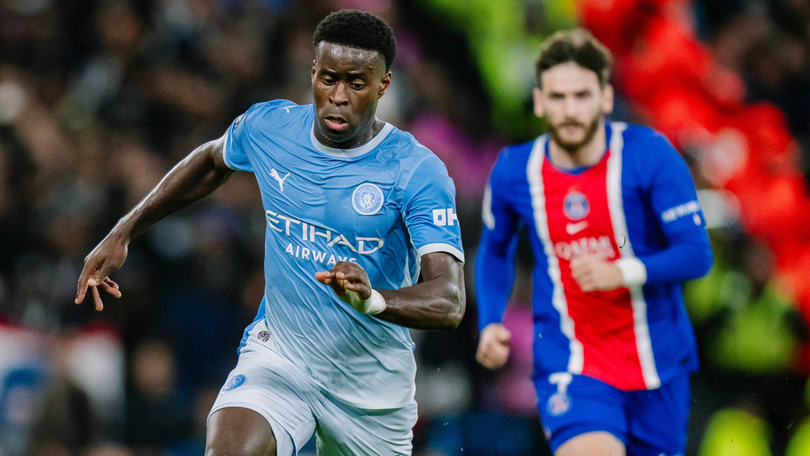 Football match action featuring a player in a Manchester City kit and another in a Paris Saint-Germain kit, both competing on the field.
